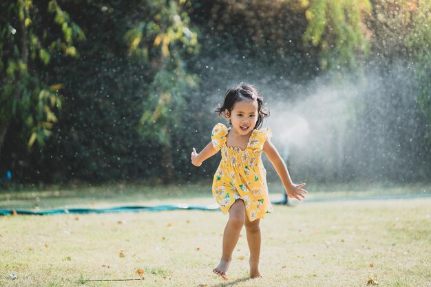 Adorable niña del sudeste asiático jugando en un césped con rociadores de agua