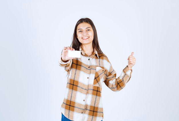 Adorable niña con tarjeta de visita dando pulgar hacia arriba en la pared blanca.