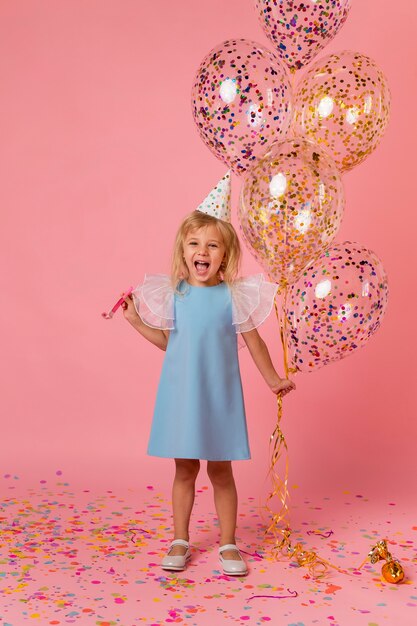 Adorable niña en traje con globos y gorro de fiesta