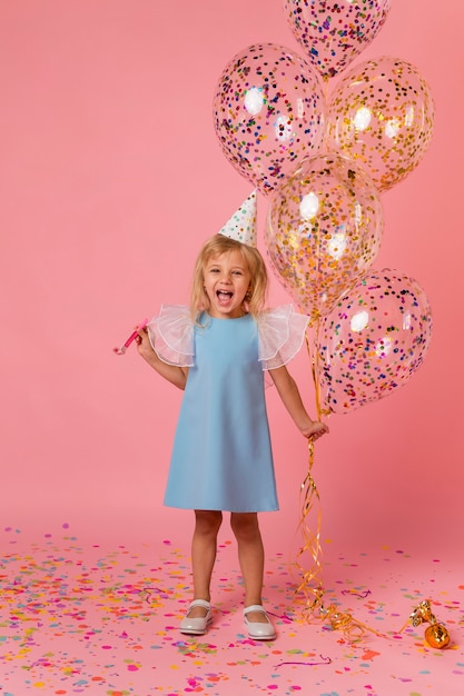 Adorable niña en traje con globos y gorro de fiesta