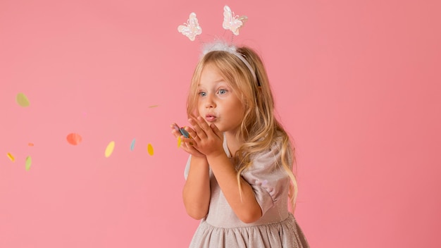 Adorable niña en traje soplando confeti