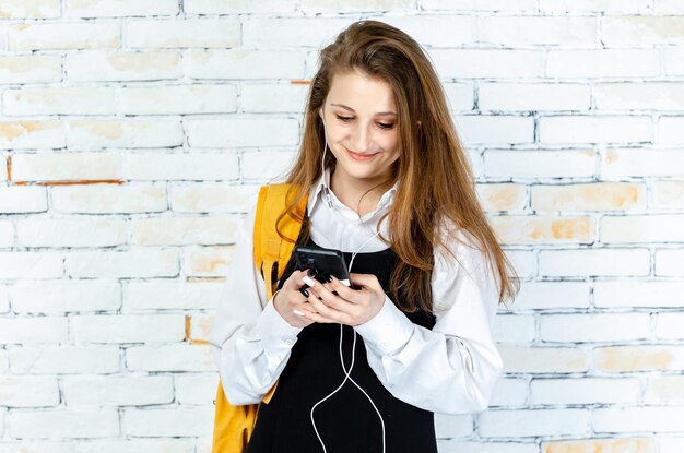 Adorable niña en uniforme escolar jugando con el teléfono en el fondo blanco Foto de alta calidad