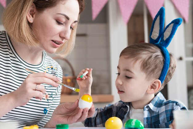 Adorable niño aprendiendo a pintar huevos para pascua