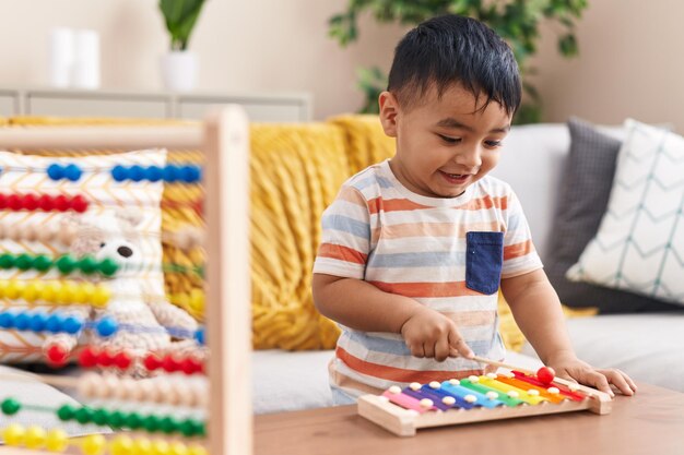 Adorable niño hispano tocando el xilófono de pie en casa