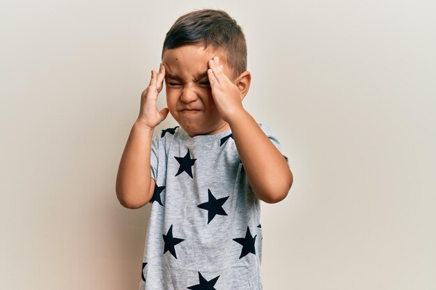 Adorable niño latino con ropa informal con dolor de cabeza en la cabeza porque el estrés sufre migraña