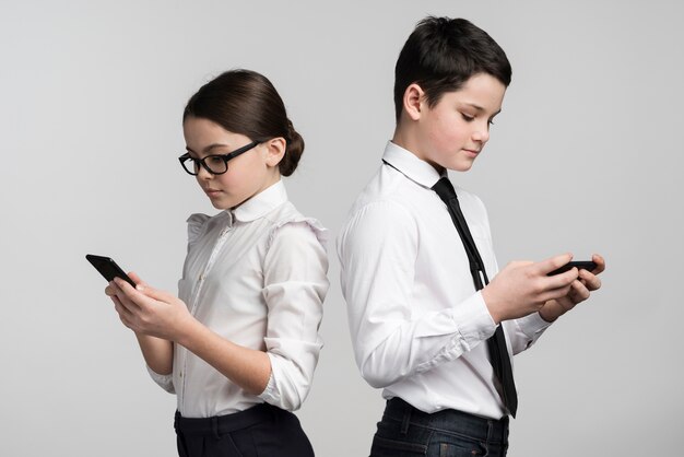 Adorable niño y niña enviando mensajes de texto en teléfonos móviles