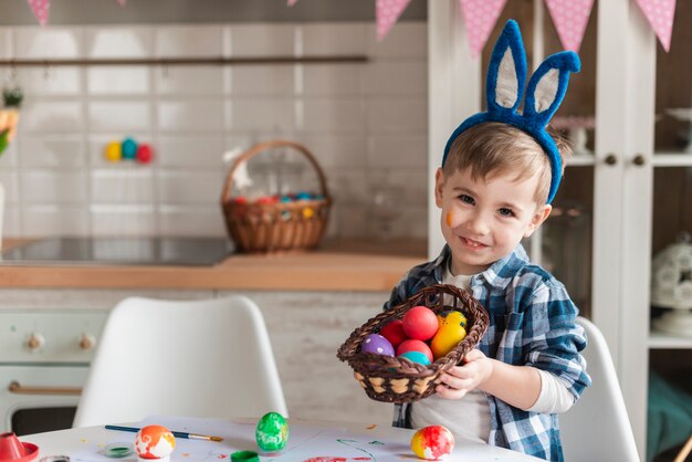 Adorable niño con orejas de conejo sosteniendo una canasta con huevos