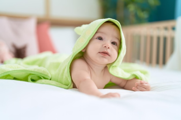 Adorable niño pequeño acostado en la cama cubierto con una toalla divertida en el dormitorio