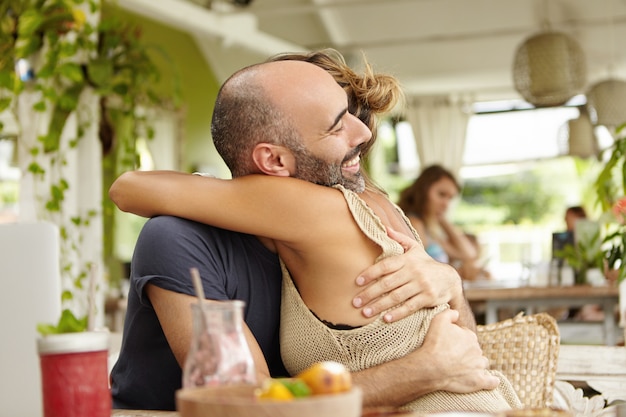 Adorable pareja disfrutando de estar juntos, abrazándose tiernamente. Elegante mujer abrazando a su novio barbudo, felicitándolo por la promoción en el trabajo.