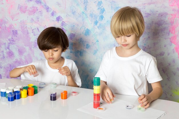 Adorables niños con camisetas blancas jugando con pinturas multicolores