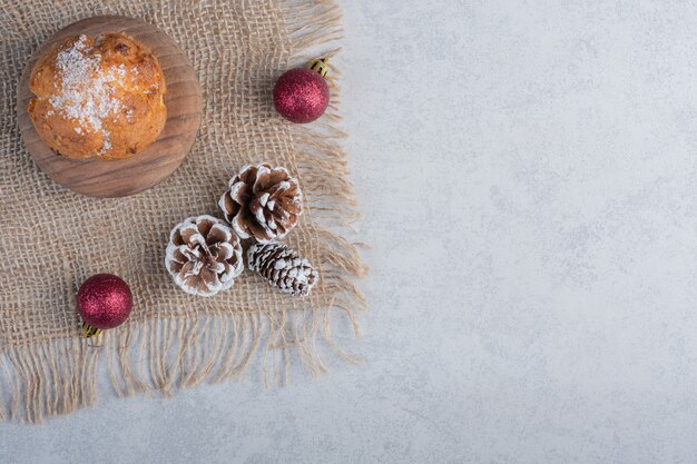 Adornos navideños y un cupcake sobre un trozo de tela sobre la superficie de mármol