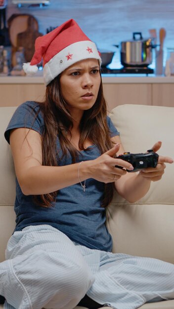 Adulto infeliz perdiendo en videojuegos con joystick en la consola de televisión. Mujer jugando juegos en línea usando el controlador en la televisión en la víspera de Navidad para la celebración navideña. Persona festiva