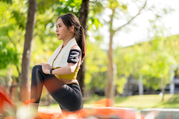 Adulto joven asiático alegre Atractiva y fuerte mañana estirándose antes de correr en el parque Concepto deportivo Estilo de vida saludable Joven corredora de fitness estirándose antes de correr en el parque