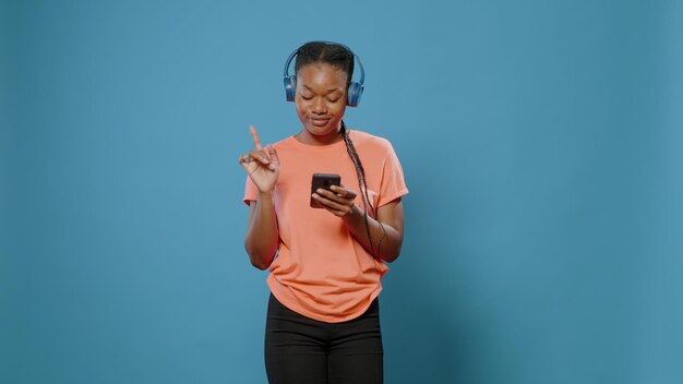 Adulto joven con auriculares haciendo movimientos de baile y usando un teléfono inteligente para cambiar de canción. Persona positiva escuchando música en los auriculares y mirando la pantalla del teléfono móvil, divirtiéndose y bailando.