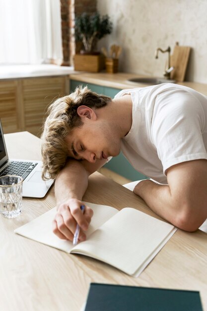 Adulto joven durmiendo mientras hace la tarea