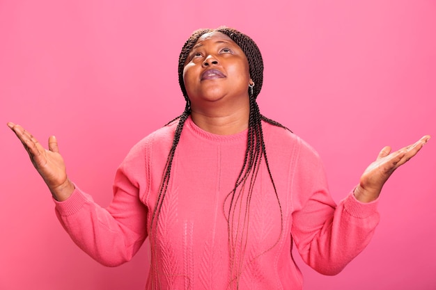 Foto gratuita adulto joven fiel con las palmas hacia el cielo suplicando y rogando perdón en el estudio. mujer afroamericana religiosa y espiritual orando por una vida mejor sobre fondo rosa