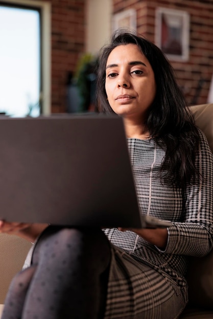 Adulto joven navegando por Internet en una computadora portátil, trabajando en un informe comercial desde casa. Usar la red en línea para investigar información para el trabajo independiente, asistir al seminario web de la escuela en línea.