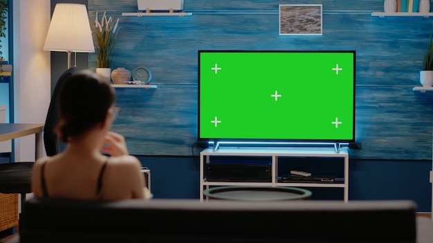 Adulto joven viendo la pantalla verde en la televisión en casa