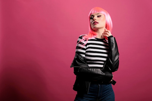 Adulto punk sensual con chaqueta de cuero rockero en el estudio, expresando un estilo de moda funky despreocupado. Atractiva dama hermosa con ropa de moda y elegante cabello rosado, lindo maquillaje.