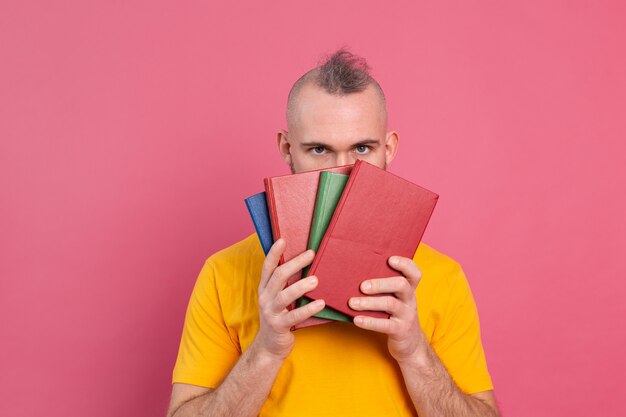 Adulto sonriente chico de ropa casual con barba abraza sus libros favoritos a sí mismo aislado en rosa