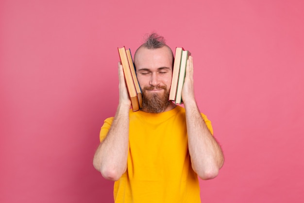Adulto sonriente chico de ropa casual con barba abraza sus libros favoritos a sí mismo aislado en rosa