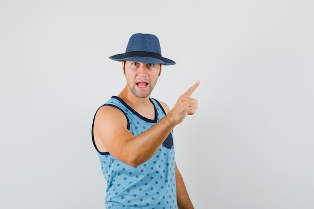 Advertencia de joven con el dedo en camiseta azul, sombrero y con enojo. vista frontal.