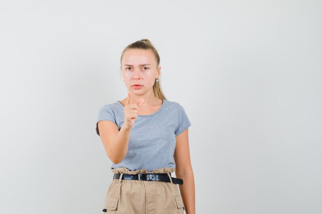 Advertencia de señorita con el dedo en camiseta y pantalón y mirando serio