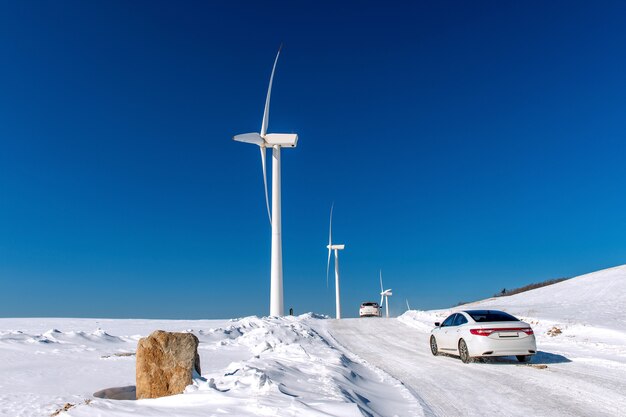 Aerogenerador y coche con cielo azul en paisaje invernal