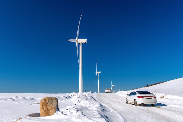 Aerogenerador y coche con cielo azul en paisaje invernal