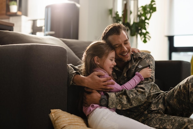 Afectuoso padre militar y su hija abrazándose con los ojos cerrados en casa