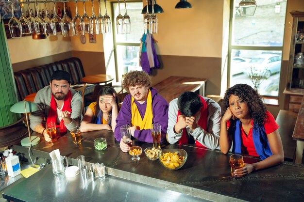 Aficionados al deporte animando en el bar, pub y bebiendo cerveza mientras ven una competición deportiva.