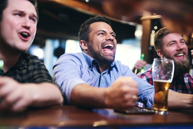 Aficionados al fútbol emocionados viendo fútbol americano en el pub