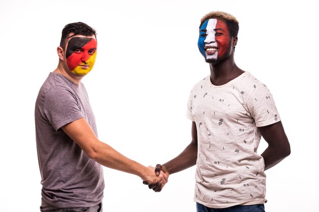 Los aficionados al fútbol de los equipos nacionales de Alemania y Francia con la cara pintada se dan la mano sobre fondo blanco.