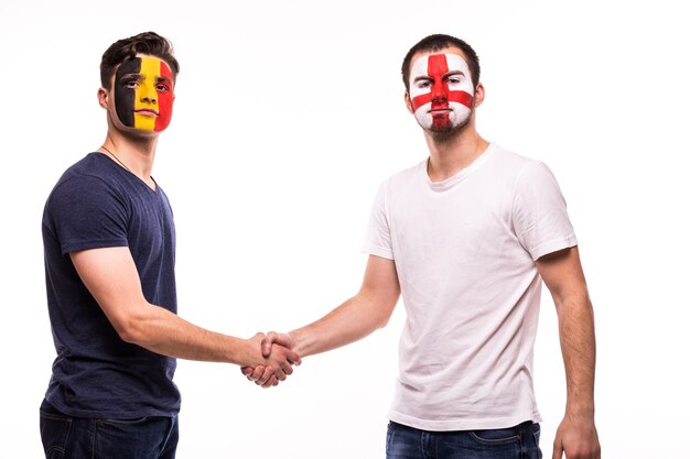 Los aficionados al fútbol de los equipos nacionales de Bélgica e Inglaterra con la cara pintada se dan la mano sobre fondo blanco.
