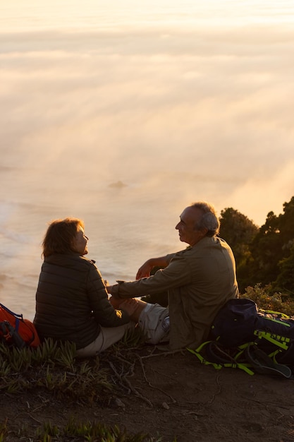 Foto gratuita aficionados a los excursionistas al atardecer. hombre y mujer con ropa informal y con municiones sentados en la cima, mirándose el uno al otro. hobby, estilo de vida activo, concepto de amor