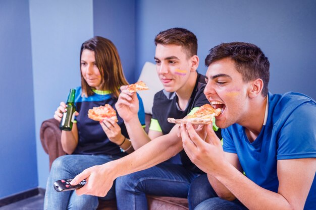 Aficionados en sofá comiendo pizza