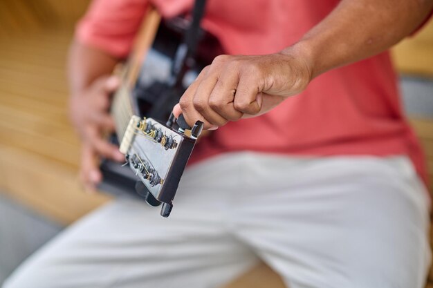 Afinación de cuerdas de guitarra. Manos masculinas experimentadas confiadas ajustando cuerdas tocando la guitarra al aire libre en un buen día, sin rostro