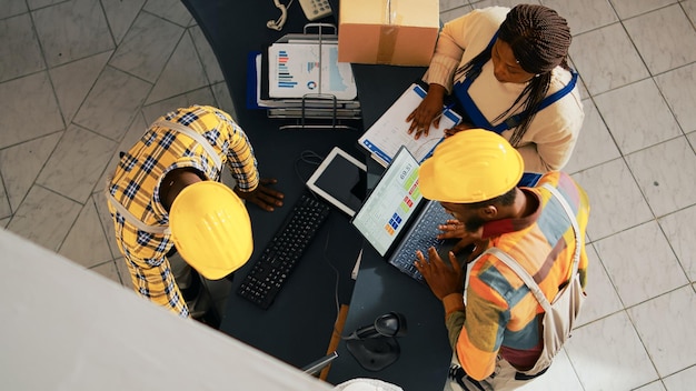 Afroamericanos mirando la lista de suministros en la PC, trabajando con la computadora para verificar el inventario y la logística. Empleados que organizan la mercancía en los estantes del espacio del almacén. Disparo de mano.