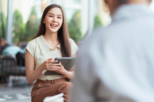 Agencia creativa asiática femenina nómada digital que trabaja en cualquier lugar discute con una amiga sobre su proyecto en un café restaurante nuevo estilo de vida laboral agencia creativa femenina asiática reunión informal cliente cliente