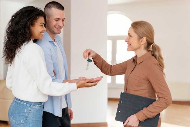 Agente de bienes raíces femenino entregando a pareja las llaves de su nuevo hogar