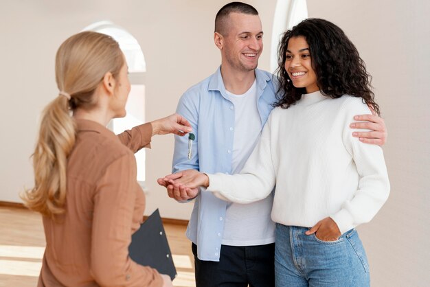 Agente de bienes raíces femenino entregando a la pareja sonriente las llaves de su nuevo hogar