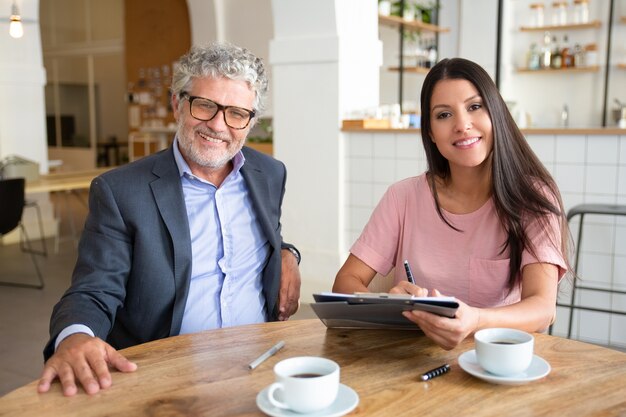 Agente y cliente reunidos con una taza de café en el coworking, sentados a la mesa, sosteniendo documentos,