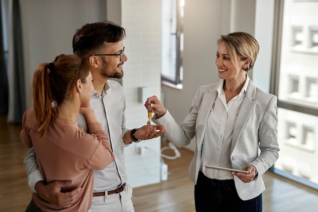 Agente inmobiliario feliz dando llaves a una pareja que está comprando su nuevo hogar