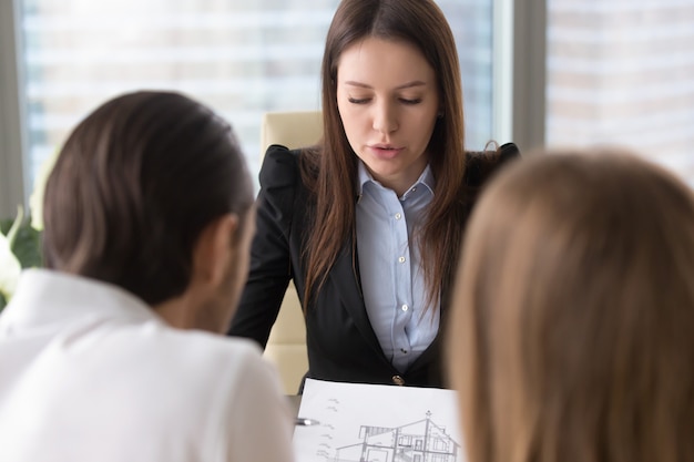 Agente inmobiliario serio femenino que discute plan de la construcción de viviendas con los clientes