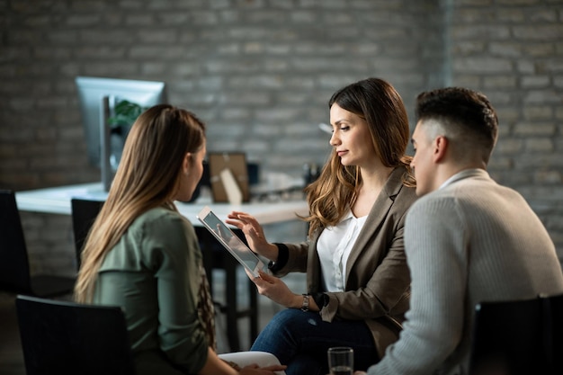 Agente de seguros que usa una tableta digital mientras se reúne con sus clientes en la oficina