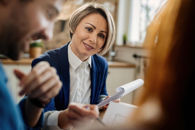 Agente de seguros sonriente revisando papeleo y comunicándose con sus clientes durante una reunión.