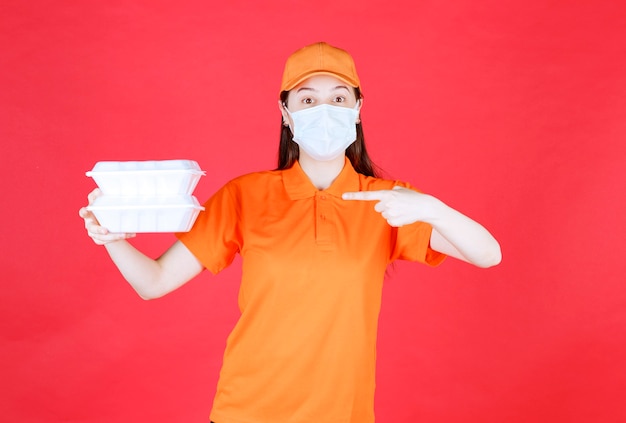 Agente de servicio femenino en código de vestimenta de color naranja y máscara sosteniendo dos paquetes de comida para llevar