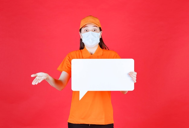 Foto gratuita agente de servicio femenino en código de vestimenta de color naranja y máscara sosteniendo un tablero de información de rectángulo blanco y parece confundida e insegura.