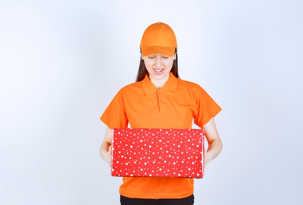 Agente de servicio femenino en código de vestimenta de color naranja sosteniendo una caja de regalo roja.