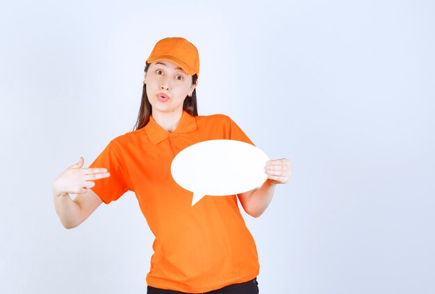 Agente de servicio femenino en código de vestimenta de color naranja sosteniendo un tablero de información ovale y parece sorprendido y aterrorizado